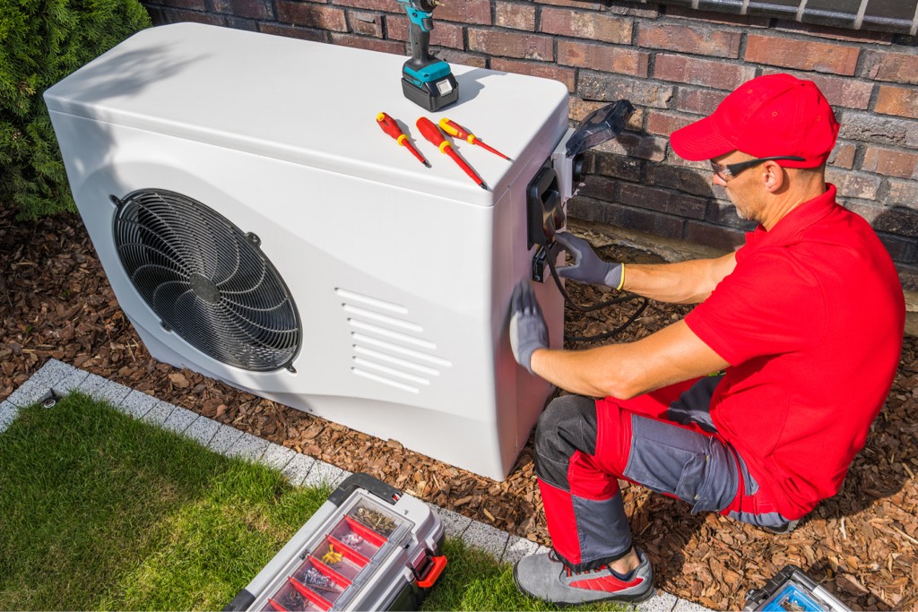 A workman installs an air source heat pump outside a property