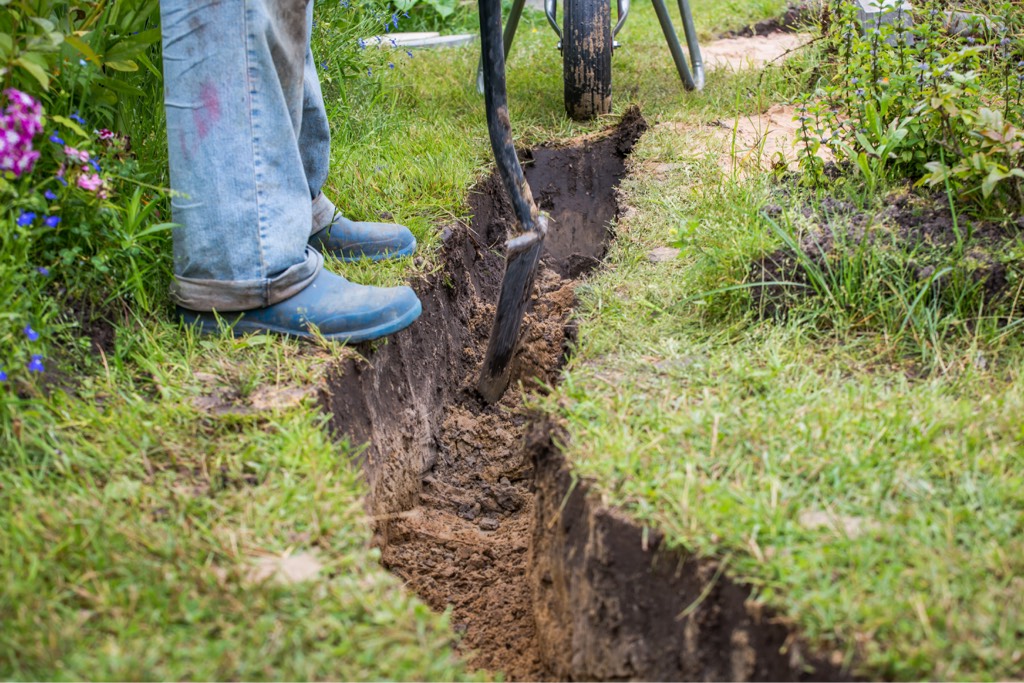 A man digs a hole in the garden to lay pipes for a ground source heat pump