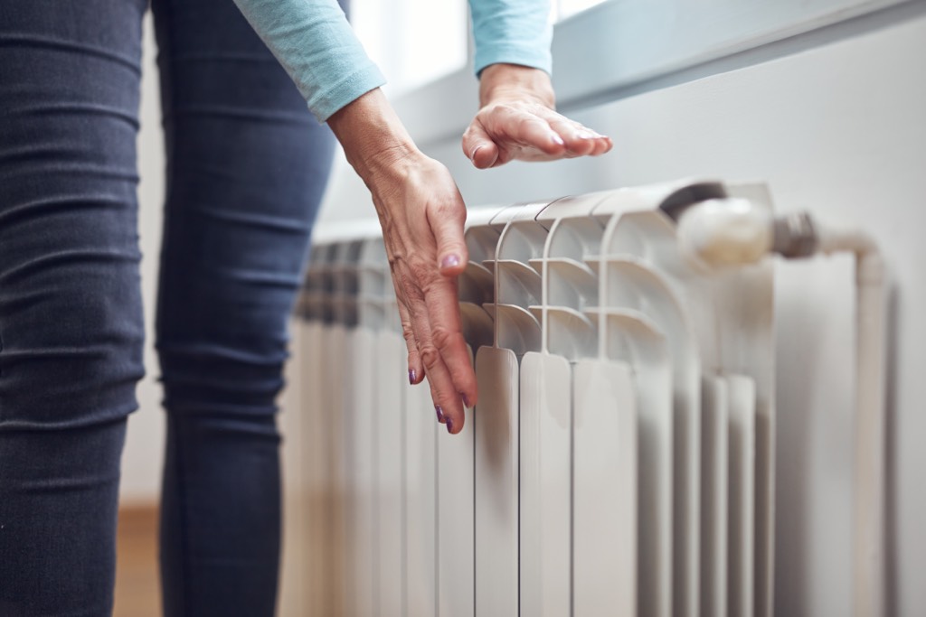 Woman touches radiator using heat pump in older home